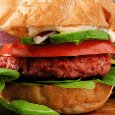 Close up of a burger with a plant based patty tomato slice green lettuce red onion and light coloured brown bun